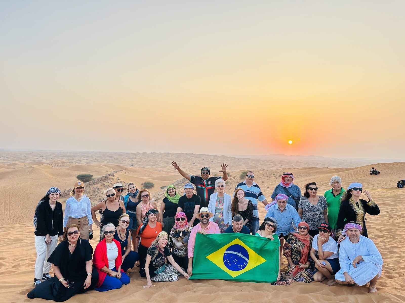 Grupo Rigue no deserto de Dubai ao pôr do sol com a bandeira do Brasil